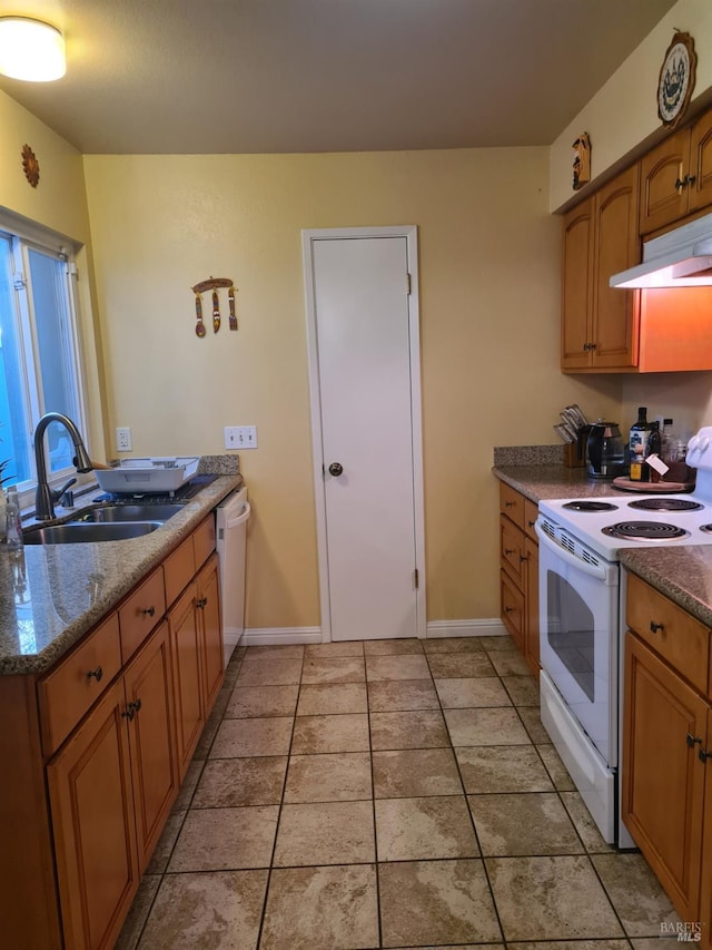 kitchen featuring white appliances, baseboards, brown cabinets, under cabinet range hood, and a sink