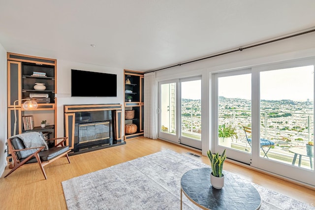living room featuring a glass covered fireplace, wood finished floors, built in shelves, and visible vents