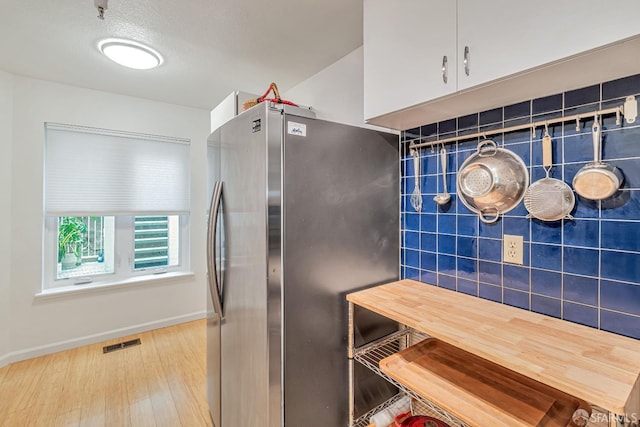 kitchen featuring visible vents, freestanding refrigerator, wood finished floors, baseboards, and white cabinetry