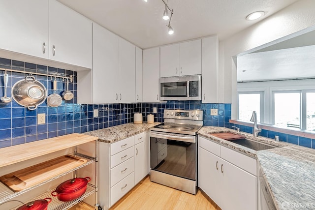 kitchen with white cabinets, a sink, light wood finished floors, stainless steel appliances, and decorative backsplash