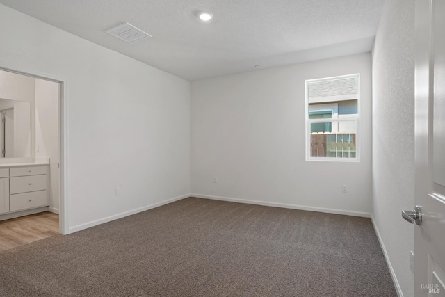 unfurnished bedroom with baseboards, a textured ceiling, visible vents, and light colored carpet