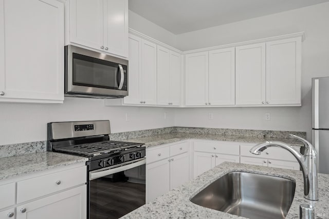 kitchen with white cabinets, light stone countertops, stainless steel appliances, and a sink