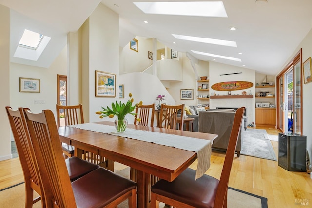 dining space featuring a fireplace, light wood-type flooring, a skylight, and high vaulted ceiling