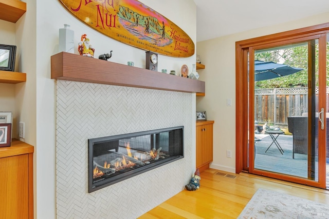 living area featuring light wood-style floors, visible vents, a glass covered fireplace, and baseboards