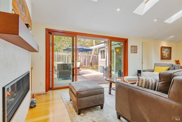 living area with light wood-style flooring, lofted ceiling with skylight, a glass covered fireplace, visible vents, and recessed lighting