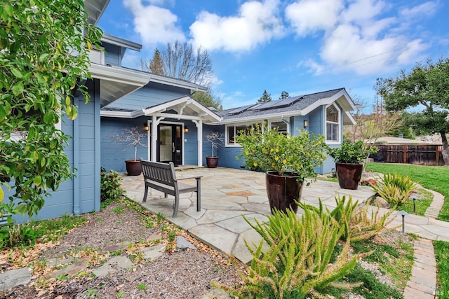 view of front of property with fence, a patio, and solar panels