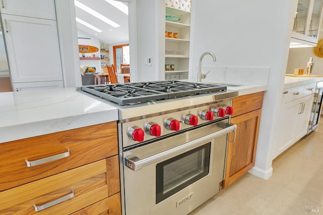 kitchen featuring a sink, premium range, vaulted ceiling with skylight, light stone counters, and light tile patterned floors