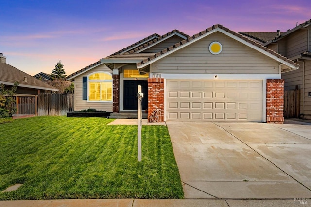 view of front of house with brick siding, a lawn, driveway, and fence