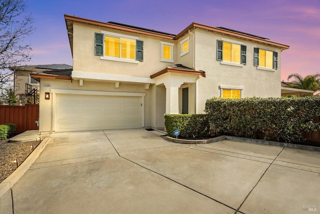 view of front of home featuring driveway, roof mounted solar panels, fence, and stucco siding