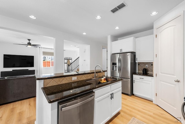 kitchen featuring stainless steel appliances, visible vents, a sink, dark stone countertops, and light wood-type flooring