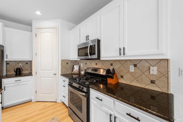 kitchen with tasteful backsplash, dark stone countertops, stainless steel appliances, light wood-style floors, and white cabinetry