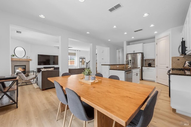 dining space featuring a glass covered fireplace, visible vents, light wood-style flooring, and recessed lighting