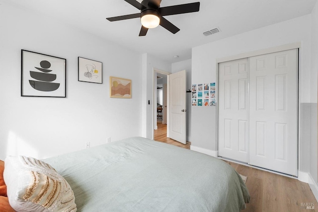 bedroom featuring wood finished floors, visible vents, baseboards, a ceiling fan, and a closet