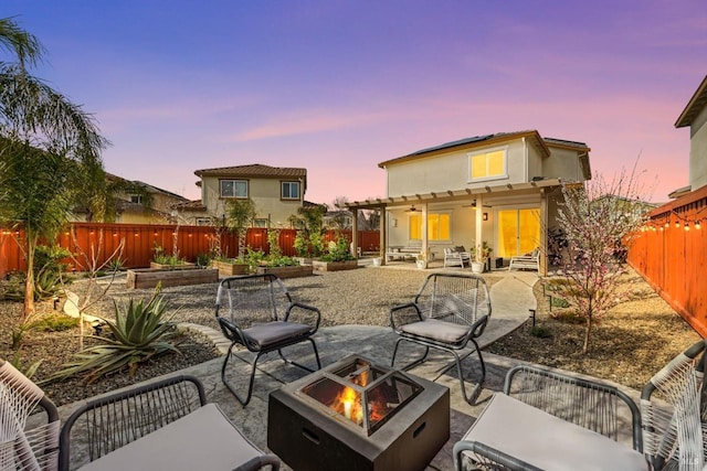 back of property at dusk featuring an outdoor fire pit, a vegetable garden, a patio, a fenced backyard, and roof mounted solar panels