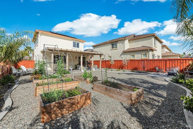 back of house featuring a vegetable garden, solar panels, a patio, a fenced backyard, and stucco siding