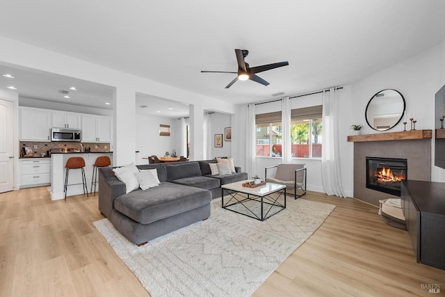 living room with light wood-style floors, a glass covered fireplace, ceiling fan, and recessed lighting