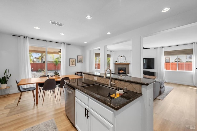 kitchen featuring a wealth of natural light, a glass covered fireplace, a sink, and stainless steel dishwasher