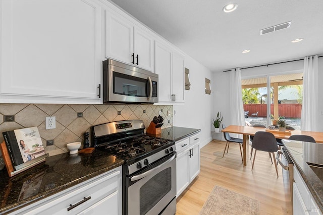 kitchen with light wood finished floors, visible vents, white cabinets, dark stone countertops, and stainless steel appliances