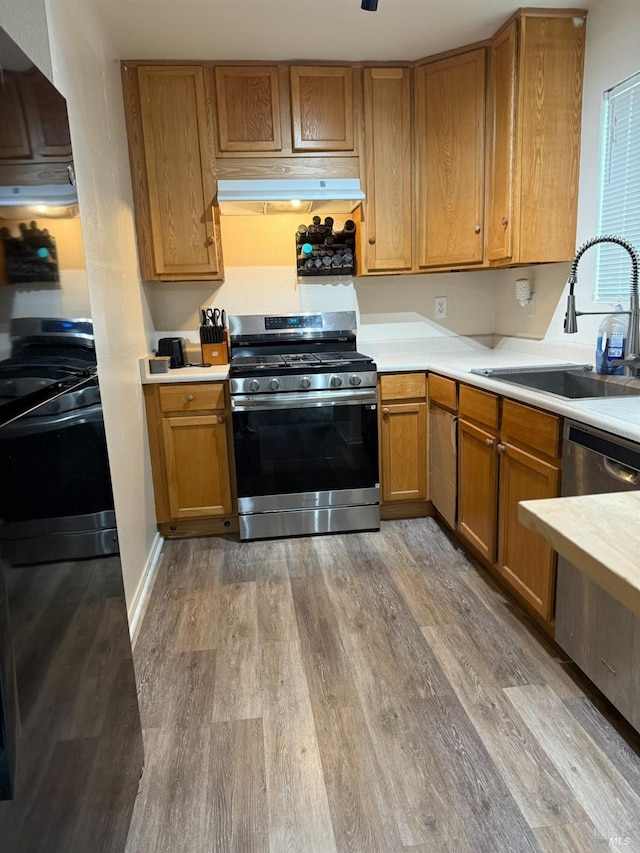 kitchen featuring under cabinet range hood, light wood-style floors, stainless steel appliances, and a sink