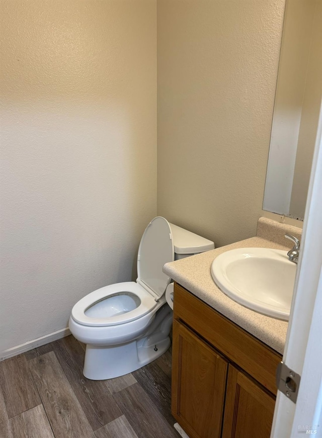 half bath with toilet, wood finished floors, vanity, and baseboards