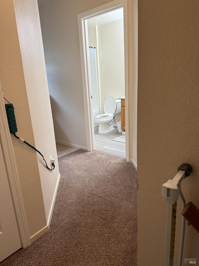 hallway featuring carpet flooring, a textured wall, and baseboards