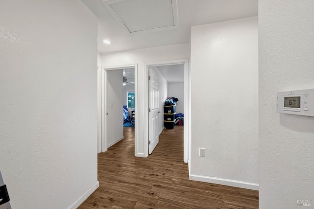 hallway featuring attic access, a textured wall, baseboards, and wood finished floors