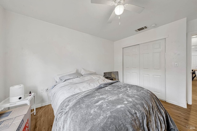 bedroom with a closet, wood finished floors, visible vents, and baseboards