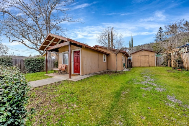 view of side of home featuring a patio area, a fenced backyard, an outbuilding, and a yard