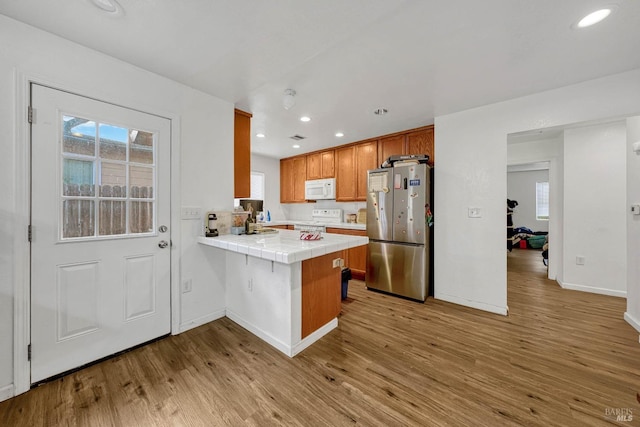 kitchen featuring range with electric cooktop, tile countertops, white microwave, freestanding refrigerator, and a peninsula