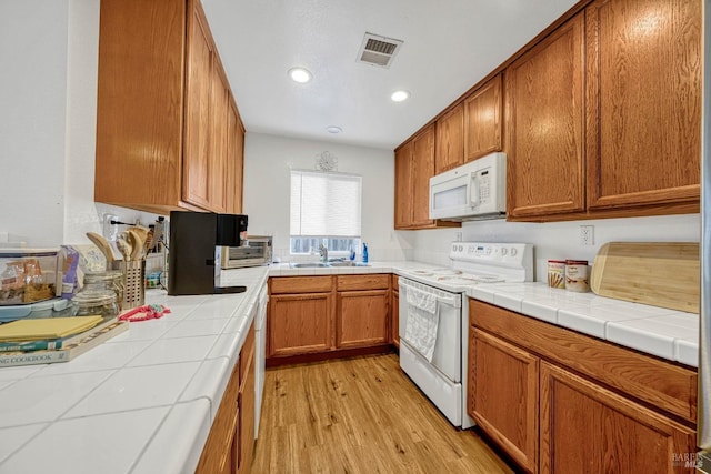 kitchen featuring visible vents, light wood-style flooring, brown cabinetry, a sink, and white appliances