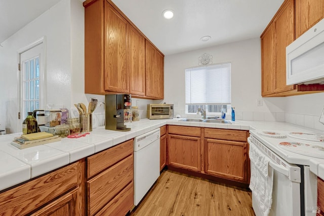 kitchen featuring white appliances, light wood-style flooring, brown cabinets, and a sink