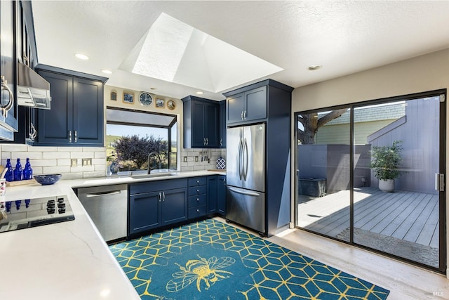 kitchen with range hood, light stone counters, a sink, appliances with stainless steel finishes, and tasteful backsplash