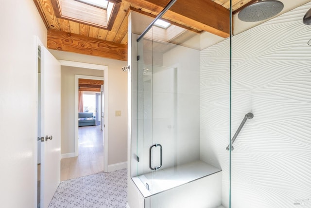 bathroom featuring tile patterned floors, a stall shower, a skylight, and baseboards