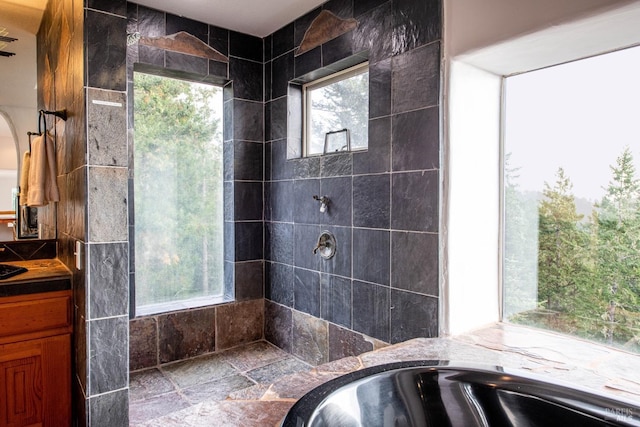 full bathroom with tiled shower, vanity, and stone tile floors