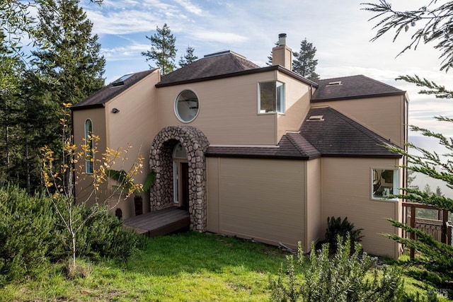 exterior space with roof with shingles, a chimney, and a front yard