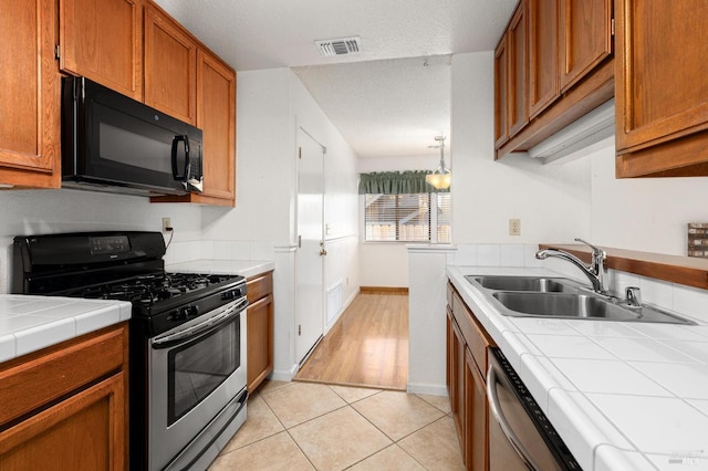 kitchen featuring tile countertops, light tile patterned flooring, a sink, visible vents, and appliances with stainless steel finishes