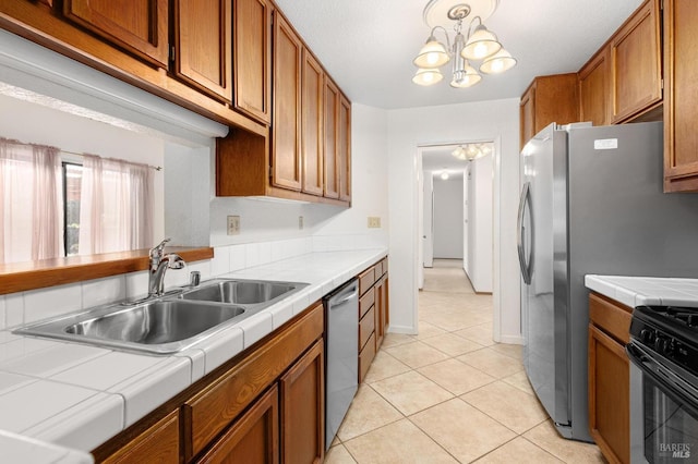 kitchen featuring tile counters, dishwasher, brown cabinets, an inviting chandelier, and a sink