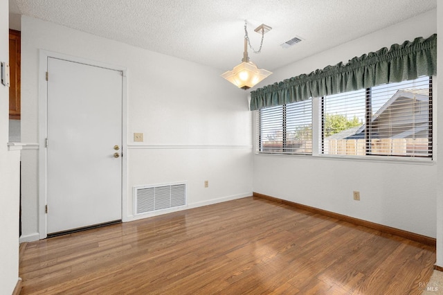 unfurnished room with baseboards, visible vents, light wood-style flooring, and a textured ceiling