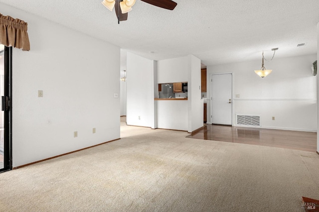 unfurnished living room with light carpet, baseboards, visible vents, a ceiling fan, and a textured ceiling