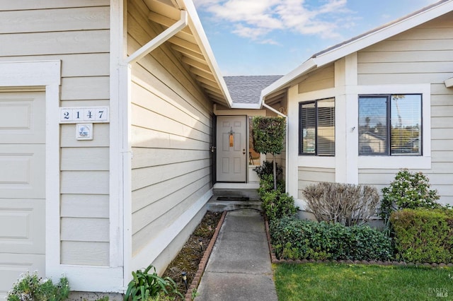 doorway to property with an attached garage and roof with shingles