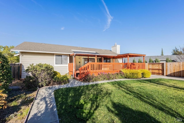 rear view of property with a deck, a yard, a chimney, and fence