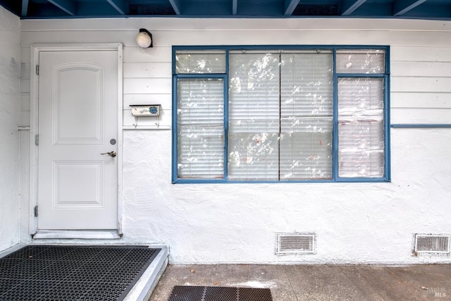 view of exterior entry with visible vents and stucco siding