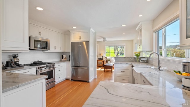 kitchen featuring high end appliances, light wood-type flooring, white cabinets, and light stone countertops