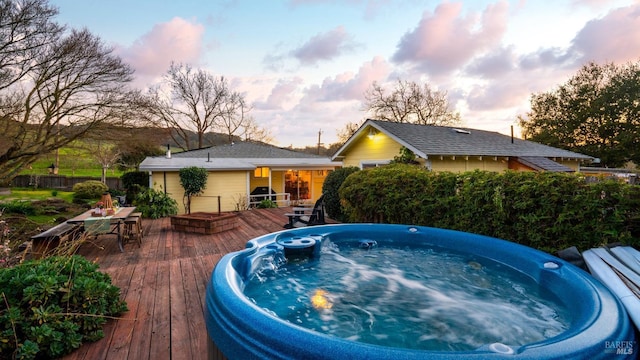 pool at dusk with outdoor dining space, hot tub deck surround, and a wooden deck