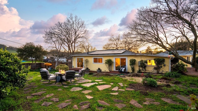 back of house at dusk featuring a fire pit, solar panels, fence, a yard, and a patio area