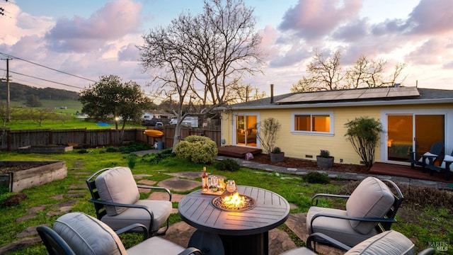 rear view of house featuring an outdoor living space with a fire pit, roof mounted solar panels, fence, a garden, and a wooden deck