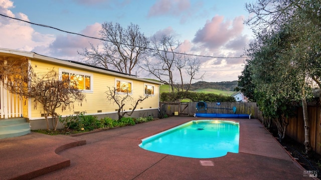 pool at dusk featuring a patio, a fenced backyard, and a fenced in pool