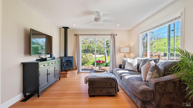 living area with ceiling fan, recessed lighting, baseboards, light wood-style floors, and a wood stove