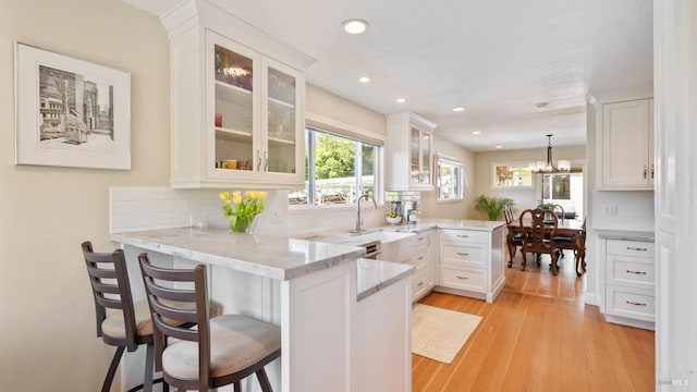 kitchen with a peninsula, white cabinetry, light stone counters, and a sink