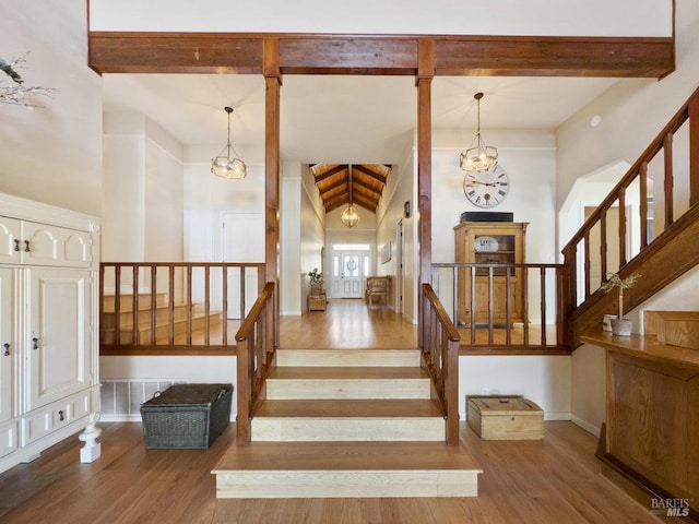 stairway with a chandelier, high vaulted ceiling, beamed ceiling, and wood finished floors